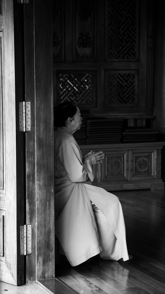 A monk sits in meditation indoors at a Vietnamese temple, deep in thought.